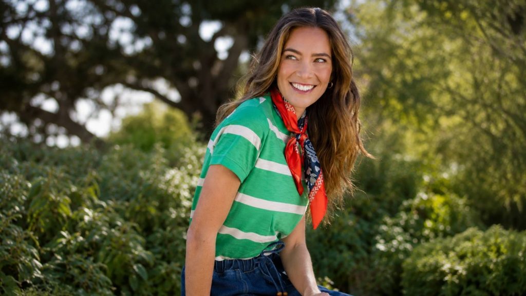 Smiling woman wearing a green striped top, red patterned scarf and blue jeans in a summer garden