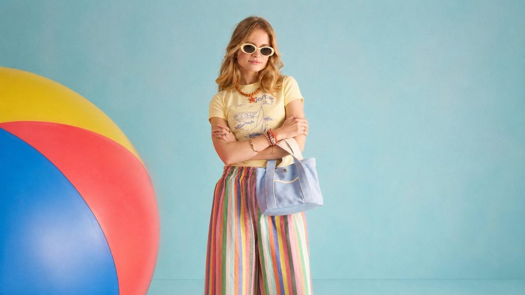 Woman wearing a yellow graphic T-shirt and colourful striped trousers against a blue background