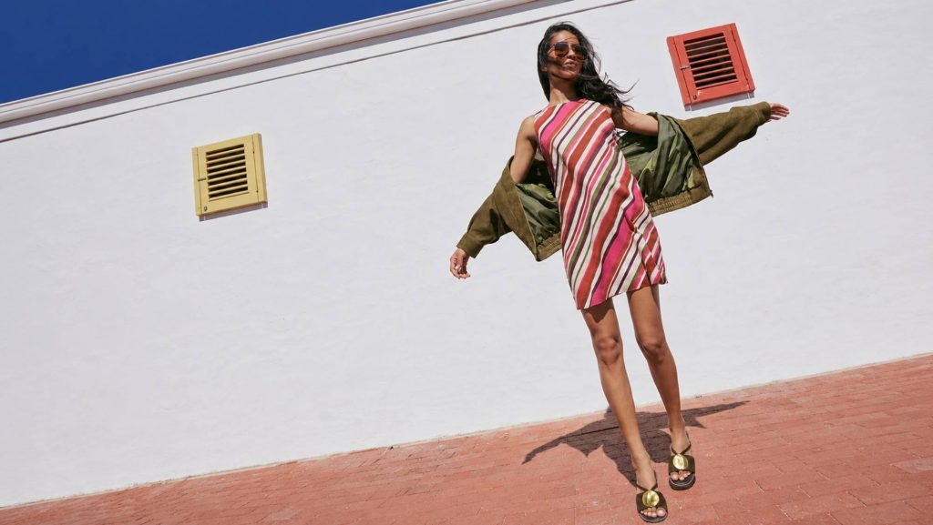 Woman wearing a colourful striped Nobody’s Child dress with an olive jacket