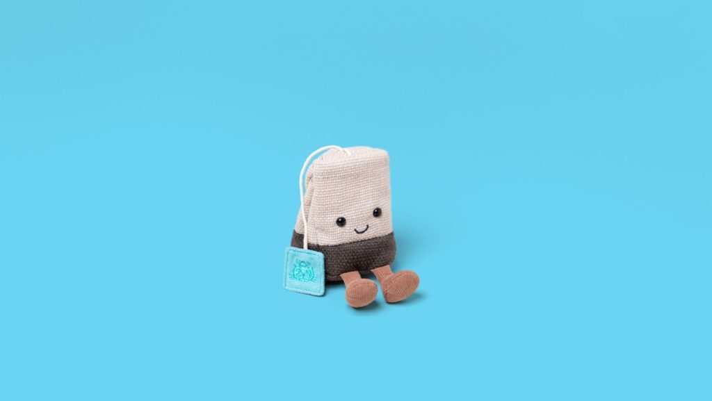 Jellycat Amuseables Steepy Tea Bag soft toy sitting against blue background