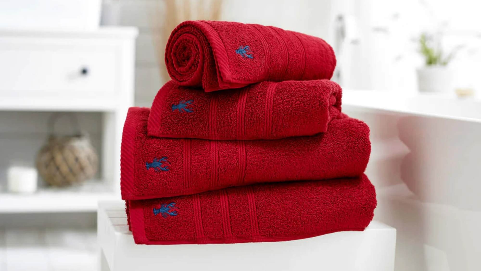 A stack of vibrant red bath towels in various sizes with an embroidered blue lobster